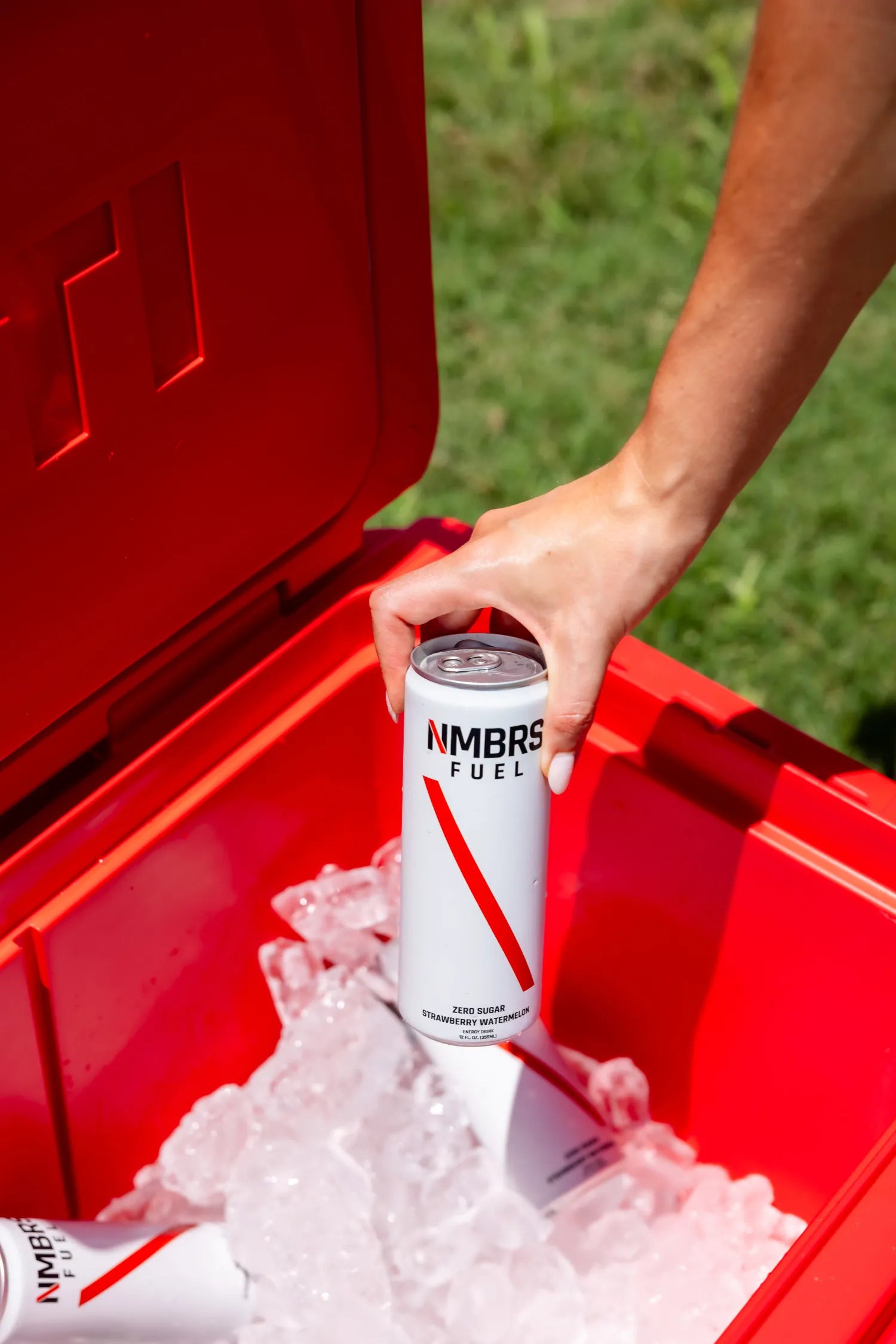 Hand placing a can of NMBRS Fuel into a red cooler with ice.