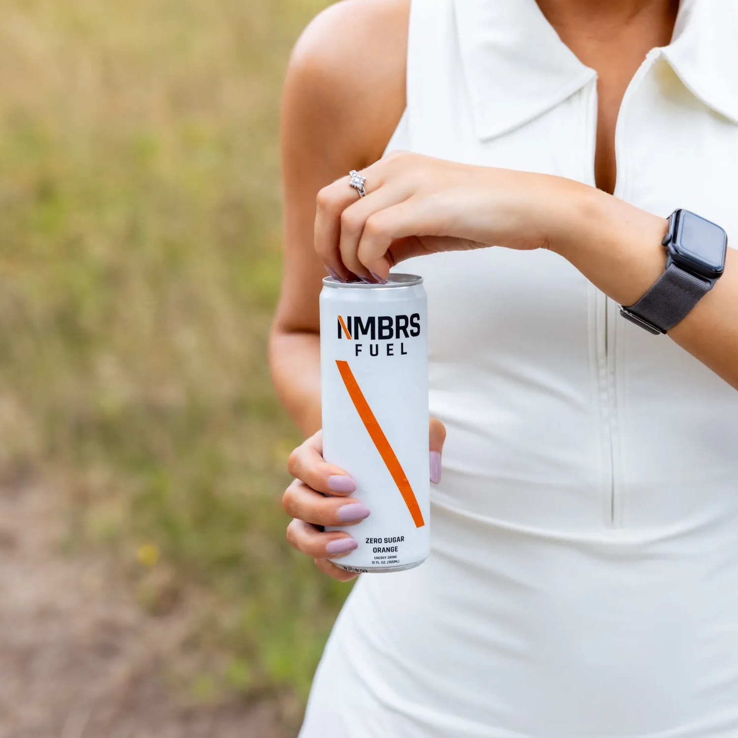 Person holding a can of NMBRS Fuel in an outdoor setting