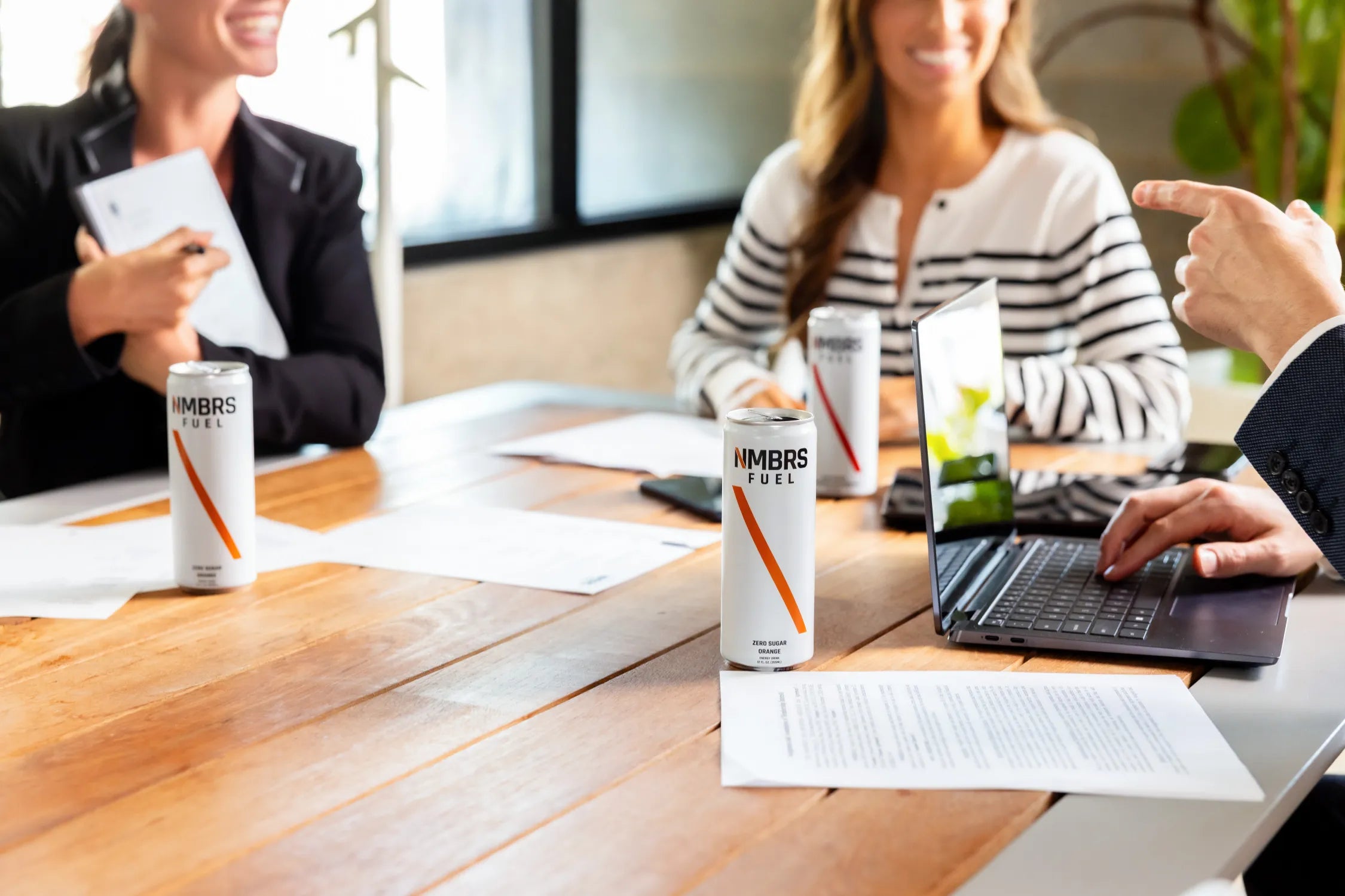People in a meeting with cans of NMBRS Fuel Energy drinks on a table.